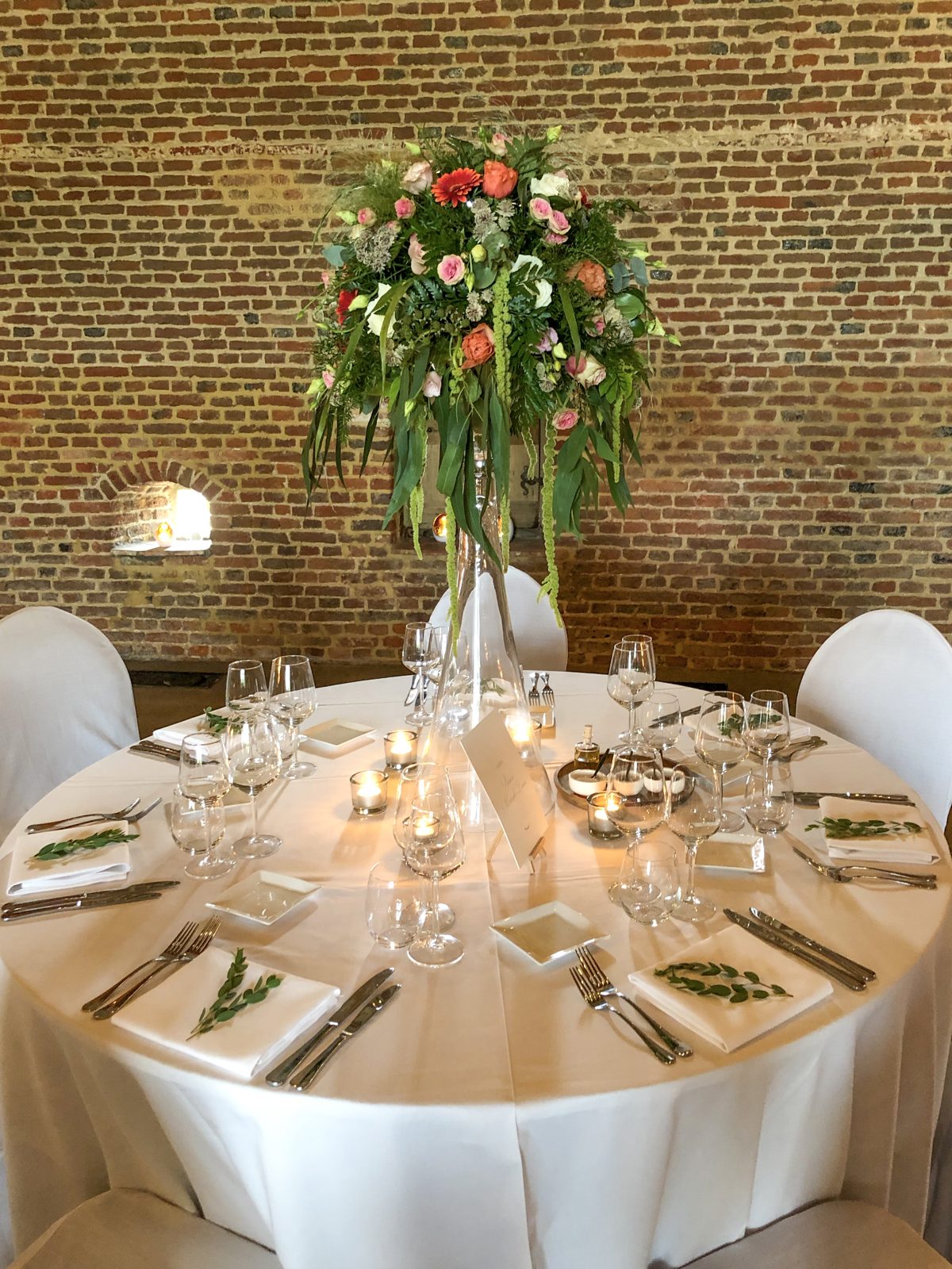 Hoog bloemstuk op glazen voet boven een gedekte tafel