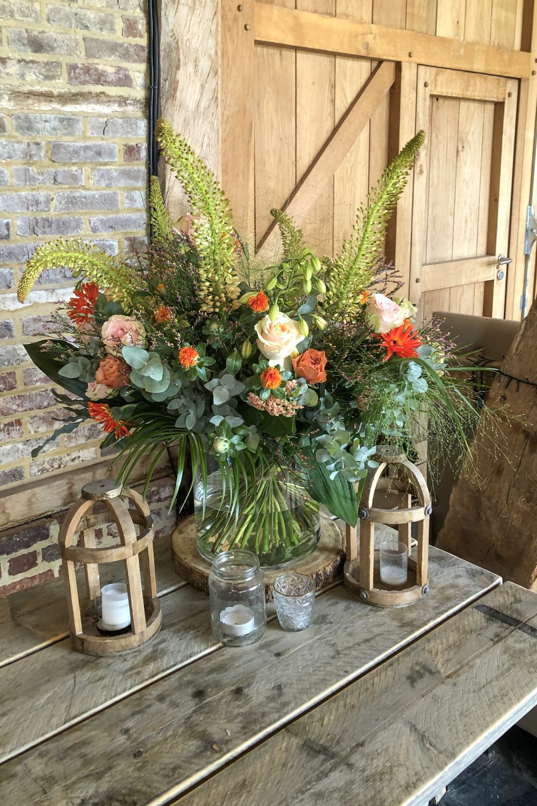 Weelderig bloemstuk met lantaarns bij een houten poort