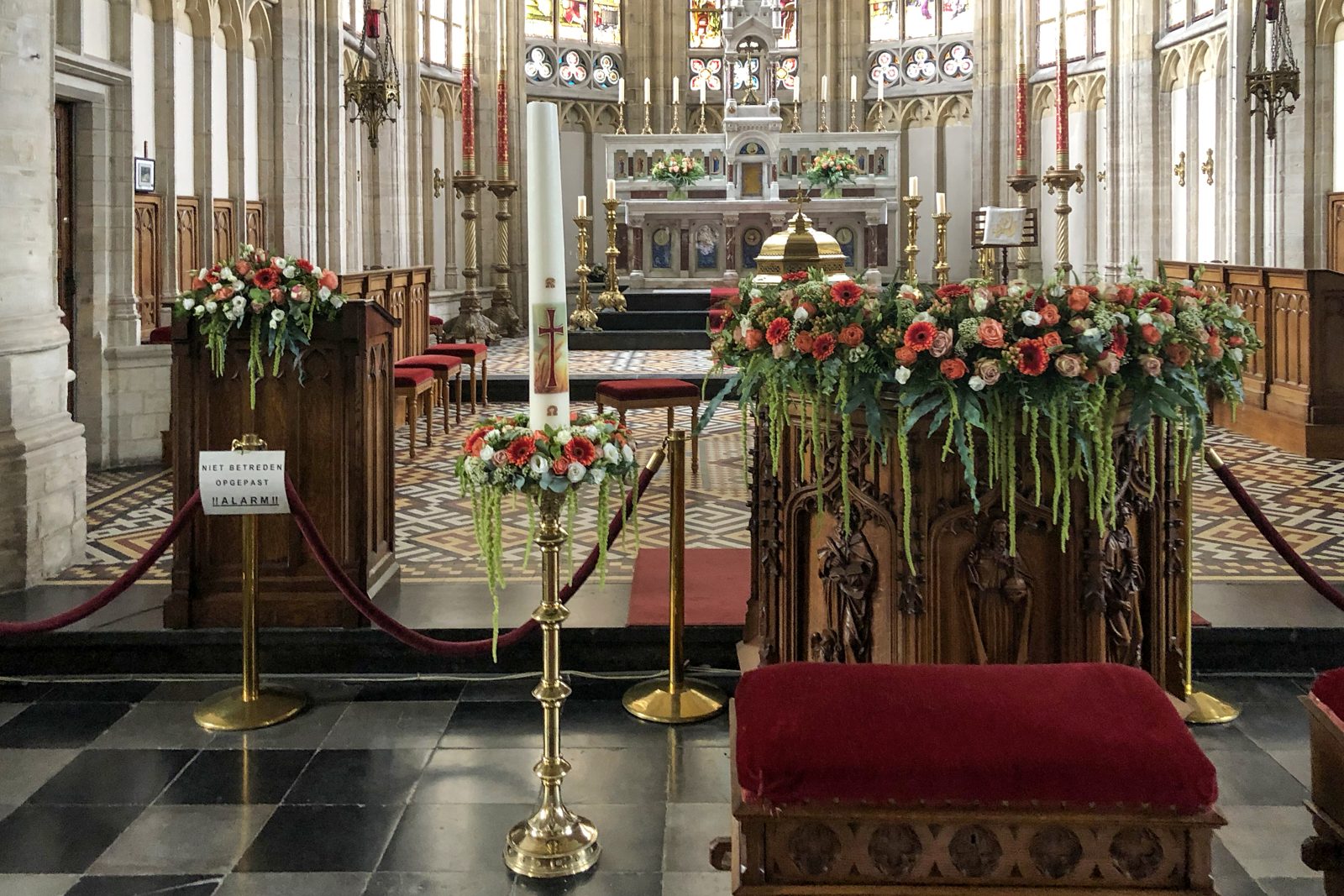 Kerkinterieur met hoge bloemstukken op kandelaars
