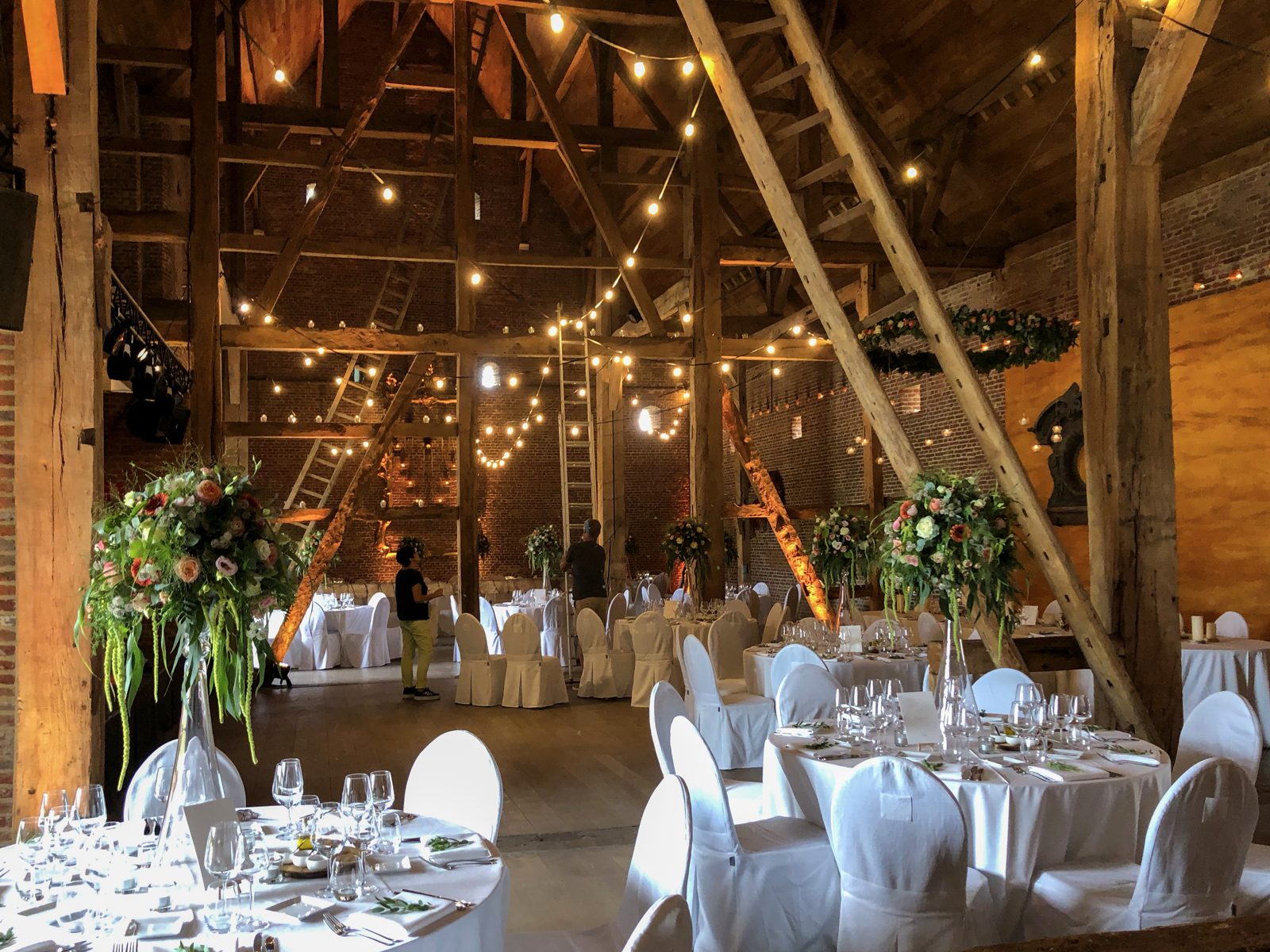Feestschuur met lichtjes en hoge bloemstukken op de tafels