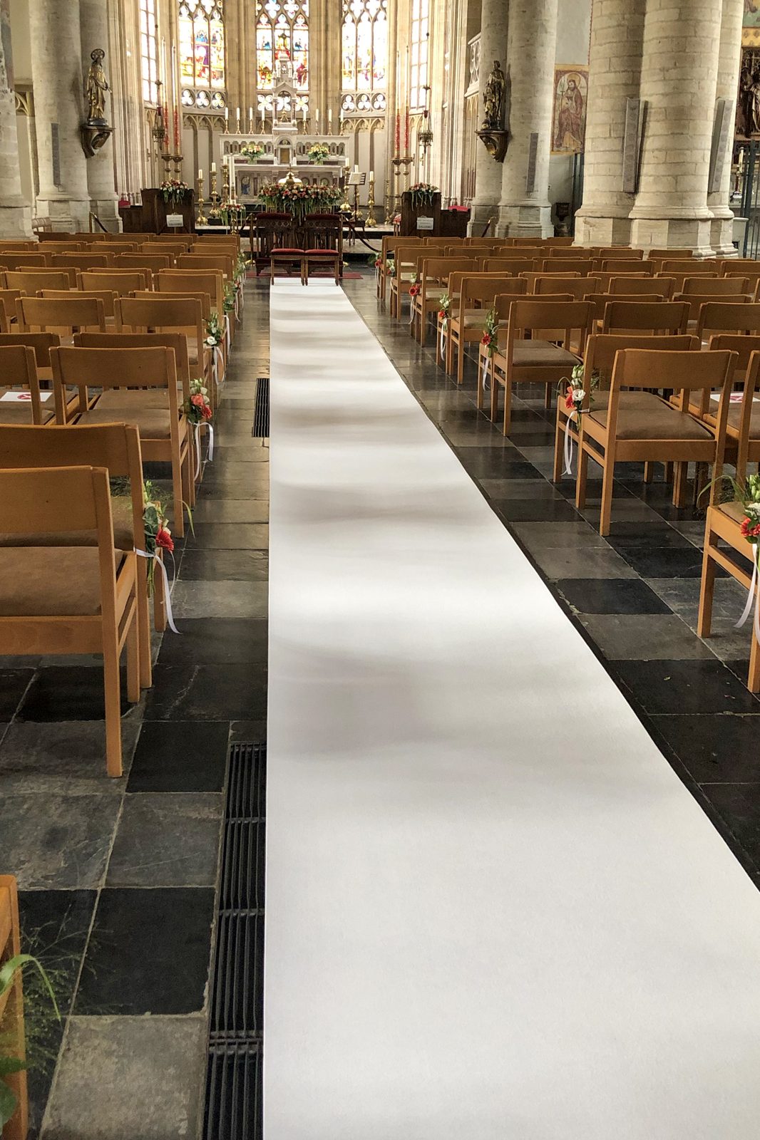 Kerkgang met witte loper en bloemen aan de banken